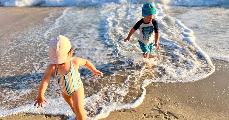 International travel with autistic kids – siblings running on a beach during family vacation.